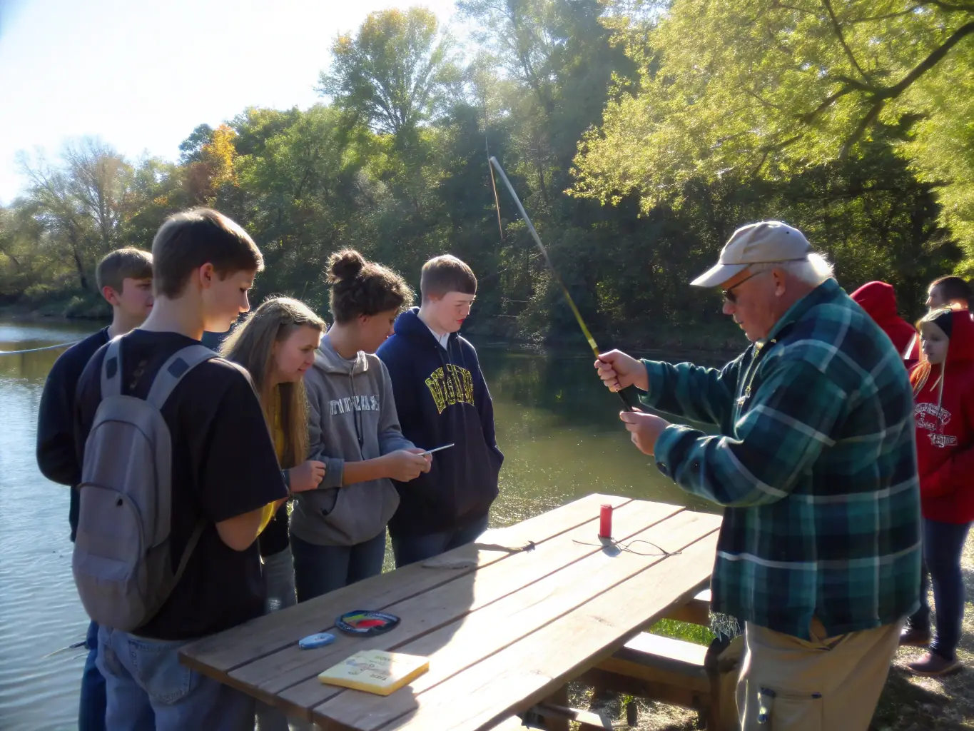 A photograph of a fishing training session, showing an instructor demonstrating casting techniques to a group of attentive participants by a riverbank. The image highlights the educational aspect of the club's activities.